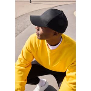A black six-panel cap made from bio cotton, worn by a person in a bright yellow sweatshirt.
