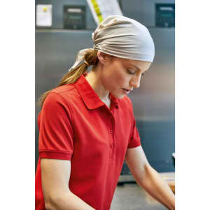 A woman with a white scarf tied back is wearing a red polo shirt while working in a kitchen setting.