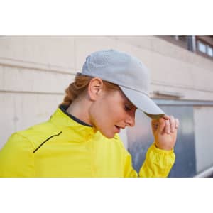A cap in light grey with a logo, worn by a person in a bright yellow jacket against an urban backdrop.