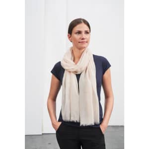 A light beige scarf draped around a woman's neck, wearing a navy top and standing against a plain background.