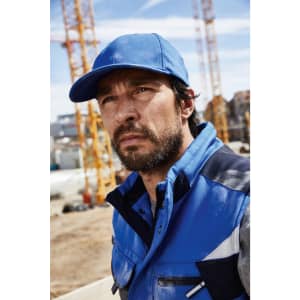 A blue 6 Panel Workwear Cap worn by a man in a blue jacket, set against a construction site background.