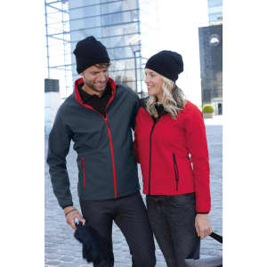 A couple outdoors, wearing a grey jacket with red accents and a black beanie, alongside a red jacket and black beanie.