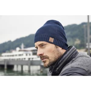 A cotton hat in navy blue worn by a man, featuring a small logo on the side, with a scenic waterfront background.