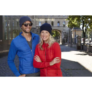 A red and a navy basic knitted beanie worn by two smiling individuals in casual jackets outdoors.
