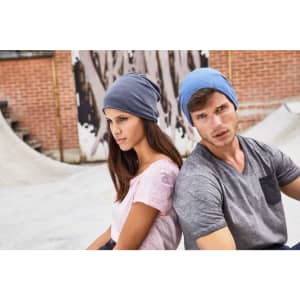 A grey and blue beanie is displayed on a male and female model in a casual setting. The background features textured walls and skate ramps.