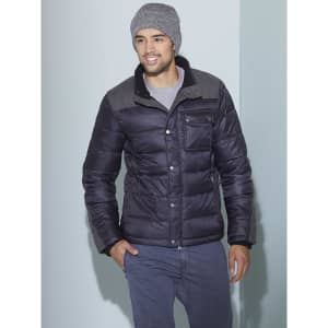 A man wearing a grey Melange beanie and a black puffer jacket, posing against a light blue wall.