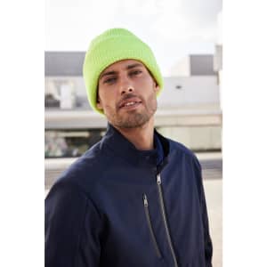 A bright yellow reflective winter beanie worn by a man in a navy jacket, set against an urban backdrop.