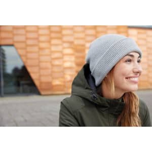 A soft grey knitted winter beanie worn by a woman with long hair, dressed in a green jacket.