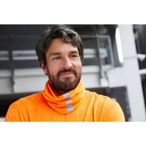 A man in an orange high-visibility shirt with reflective stripes, standing in an outdoor environment.