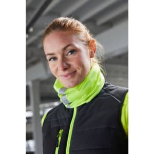A woman wearing a black vest with a bright yellow collar. She has red hair and is smiling. The background is industrial.