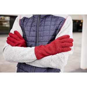 A pair of red fleece gloves worn by a person with crossed arms, dressed in a grey and navy jacket.