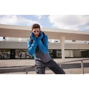 A man in a blue fleece hoodie with a grey vest stands outdoors, with a building in the background.