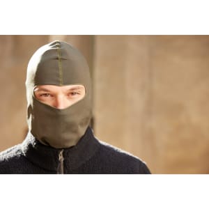 A person wearing an olive green balaclava with a zippered black fleece jacket, looking directly at the camera.