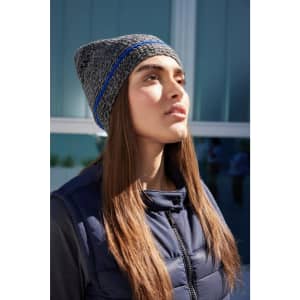 A coarse knitted beanie featuring grey and blue shades, worn by a model with long hair, against a modern backdrop.