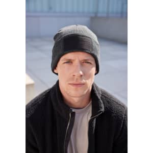 A man wearing a black beanie with a patch, paired with a dark fleece jacket, sits outdoors.
