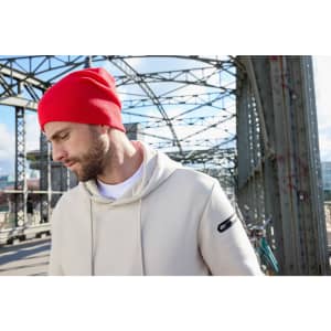 A red casual beanie displayed on a model wearing a beige hoodie, set against an industrial background.