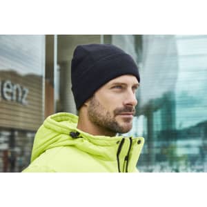 A black knitted beanie displayed on a man wearing a bright yellow jacket in an urban setting.