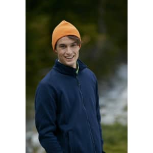 A man wearing an orange beanie and a navy blue jacket, smiling outdoors with a blurred natural background.