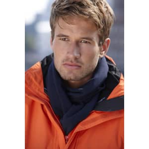 A young man wearing an orange jacket with a navy fleece scarf. The image features a blurred urban background.