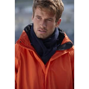 A man wearing an orange jacket and a navy fleece scarf, positioned outdoors with a blurred background.