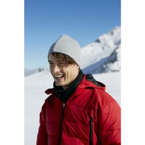 A man wearing a grey rib beanie and a red puffer jacket, smiling in a snowy mountain landscape.