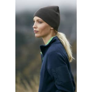 A cotton beanie in dark brown worn by a woman with blonde hair, paired with a blue jacket.