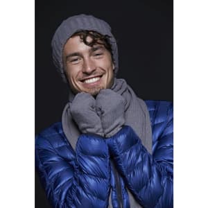 A man in a grey beanie and scarf, smiling, wearing a blue puffer jacket. The image features a logo on the scarf.