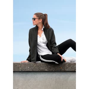 A polar fleece jacket in dark grey worn by a woman sitting casually. It features a logo and is paired with sporty attire.