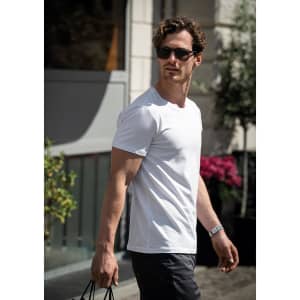 A man wearing a white T-shirt and sunglasses, walking outdoors with a bag in hand.