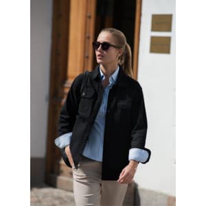 A unisex shirt in black, paired with a light blue shirt underneath, worn with sunglasses outdoors.