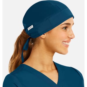A unisex scrub cap in navy blue, featuring a back tie and a logo patch, worn by a smiling individual.