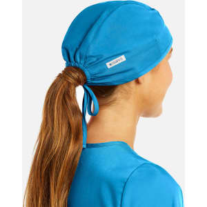 A unisex scrub cap in vibrant blue, designed with a ponytail opening at the back. Features a logo tag.