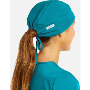A unisex scrub cap in teal with a gathered ponytail opening and a small logo tag.