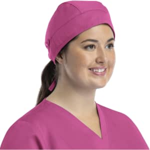 A pink unisex scrub cap with buttons, worn by a smiling woman in scrubs. The cap has a simple design and a back tie.