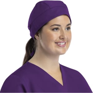 A unisex scrub cap in purple with buttons, worn by a smiling individual in scrubs.