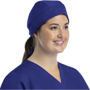 A unisex scrub cap in navy blue with buttons, worn by a smiling model.