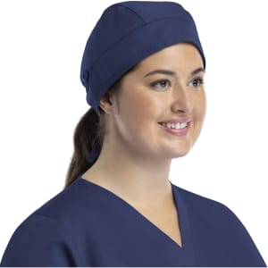 A unisex navy scrub cap with buttons, worn by a woman with long hair tied back, smiling while wearing scrubs.