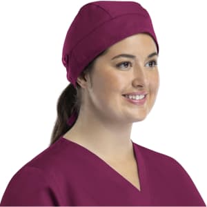 A unisex scrub cap in a rich burgundy colour with buttons, worn by a smiling woman.