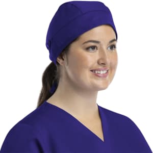 A unisex scrub cap in purple with buttons, worn by a smiling woman in a scrub top.