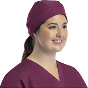 A unisex scrub cap in a rich plum colour with buttons, worn by a smiling woman in a matching top.