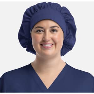 A unisex bouffant scrub cap in navy blue, featuring a logo, worn by a smiling person in a matching scrub top.