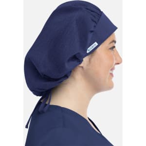 A unisex bouffant scrub cap in navy blue, featuring a logo, worn by a person from the side.