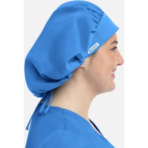 A unisex bouffant scrub cap in bright blue, worn by a model, with a logo tag visible on the side.