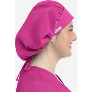 A unisex bouffant cap in vibrant pink, featuring a logo, worn on a person's head from the side.