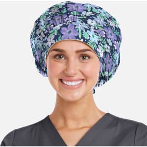 A printed unisex bouffant cap in purple with floral patterns, worn by a smiling individual in a grey scrub top.