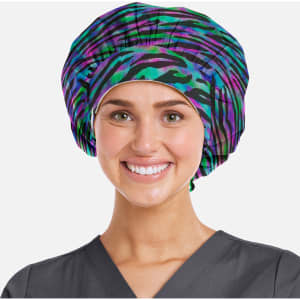 A printed unisex bouffant cap in a vibrant purple and green pattern, worn by a smiling individual in scrubs.