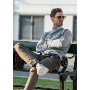 A grey sweatshirt worn by a man sitting on a bench, paired with beige trousers and sunglasses.