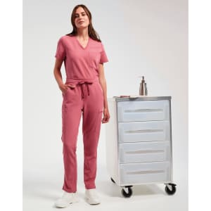 A woman wears pink cargo pants and a matching top, standing beside a mobile storage cart. The outfit features a drawstring waist.