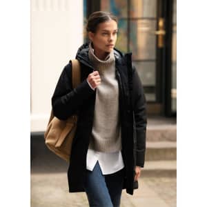 A woman in a black Northdale jacket, wearing a grey sweater and carrying a tan bag, walking outdoors.