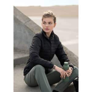 A woman in a black puffer jacket and green pants sits on a step, holding a green drink bottle.